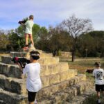 Enfants jouant au Laser Game autour d’une pyramide en pierre, se cachant et visant avec leurs fusils laser.